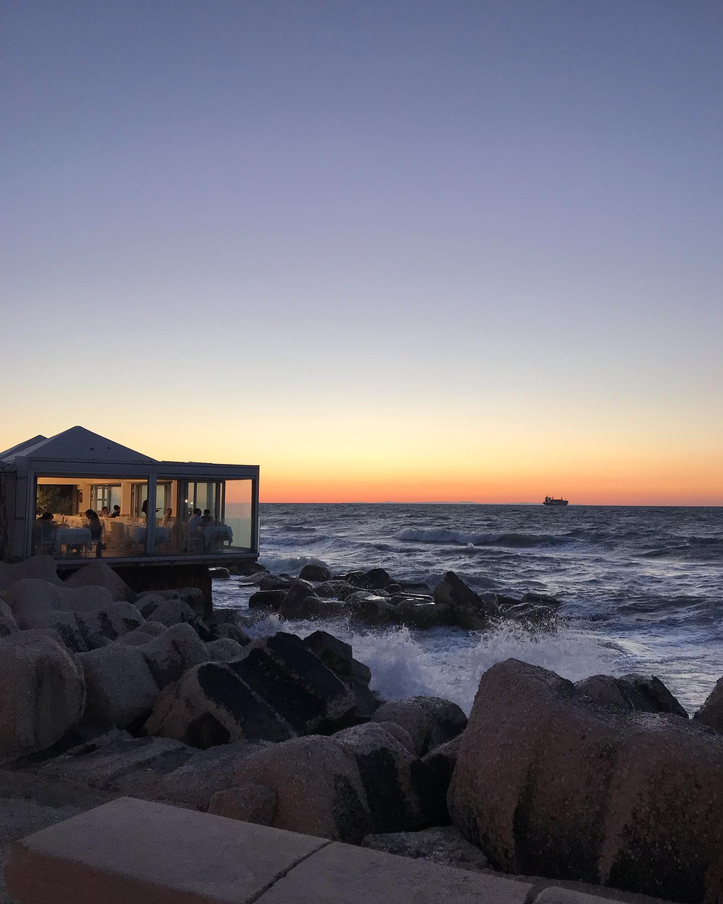 un ristorante sugli scogli fotografato al tramonto, con le onde mosse dal maestrale