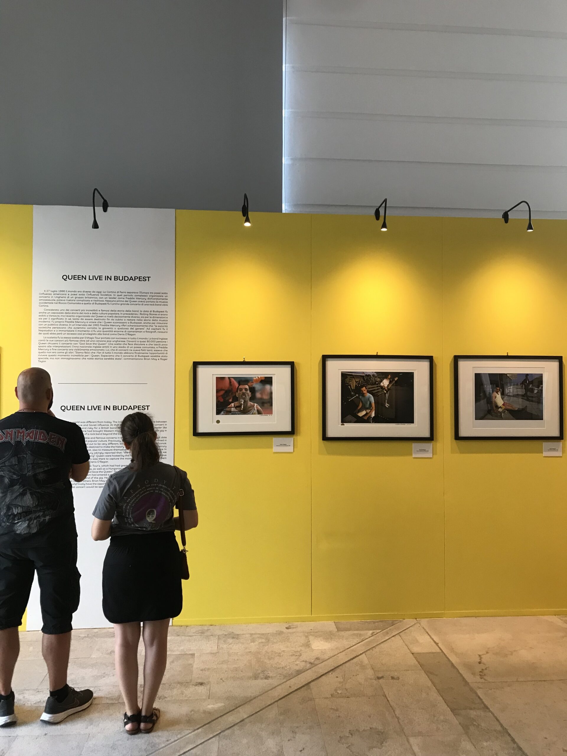 Un ragazzo e una ragazza guardano foto dei queen appese su un muro per una mostra, Queen a Budapest.